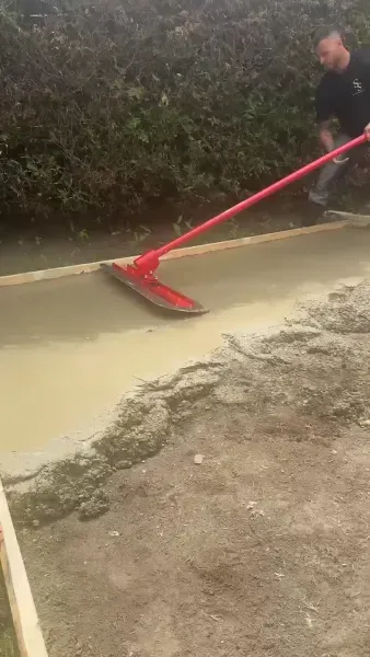 Worker leveling concrete mix across the slab with a bull float